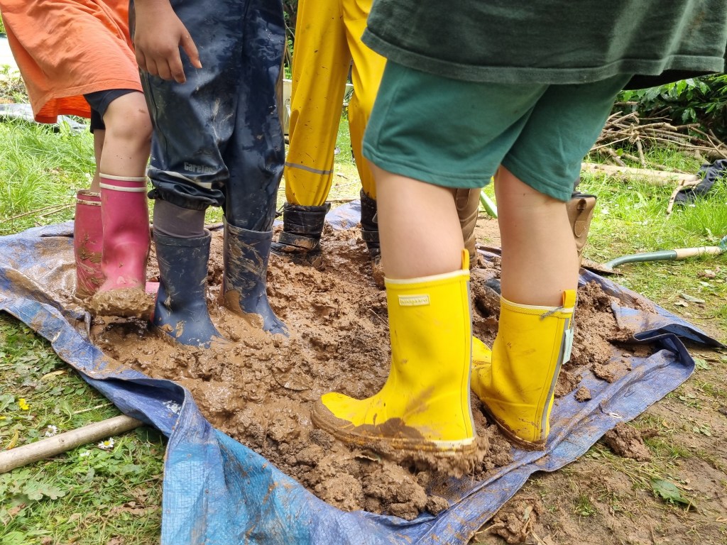 feet, wearing wellies, treading mud, straw and sand to make cob